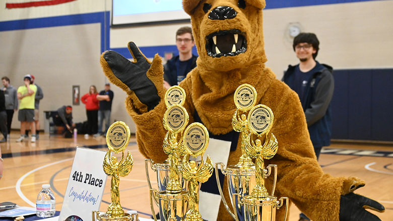 The Nittany Lion standing behind a table of trophies.