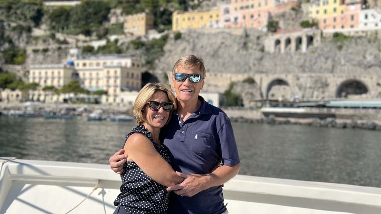 A woman and a man on a boat with the coastline behind them