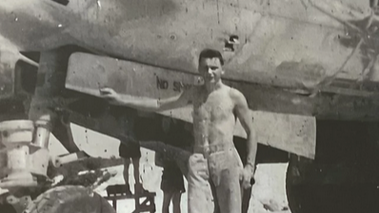 A black-and-white image of a man standing next to a plane with the words "Enola Gay" on its side