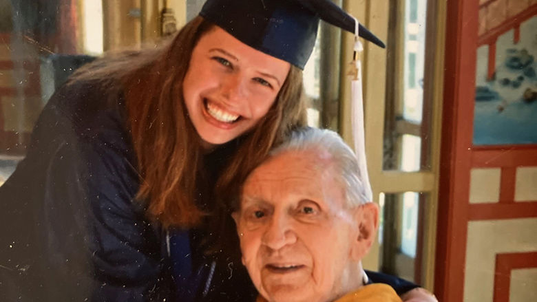 A woman in graduation regalia embraces her grandfather, also in regalia