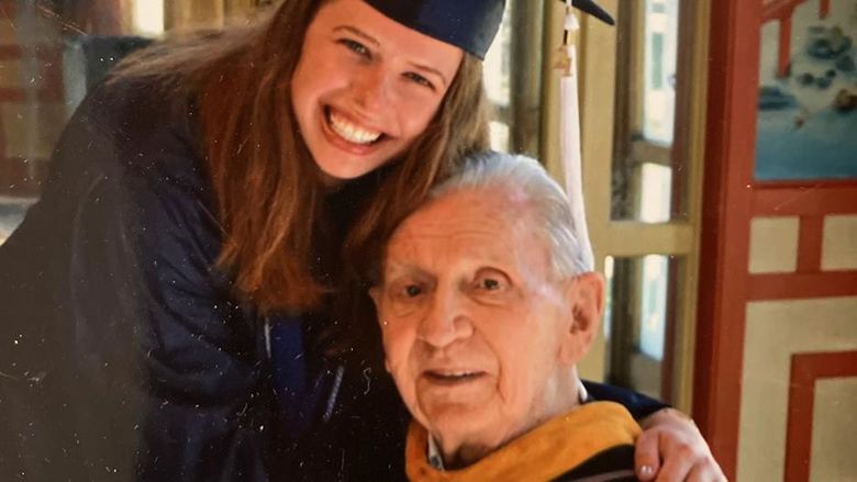 A woman in graduation regalia embraces her grandfather, also in regalia