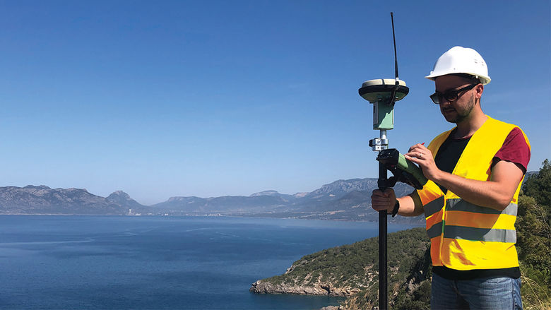 Surveyor standing with his equipment outside overlooking a wide blue sky and body of water