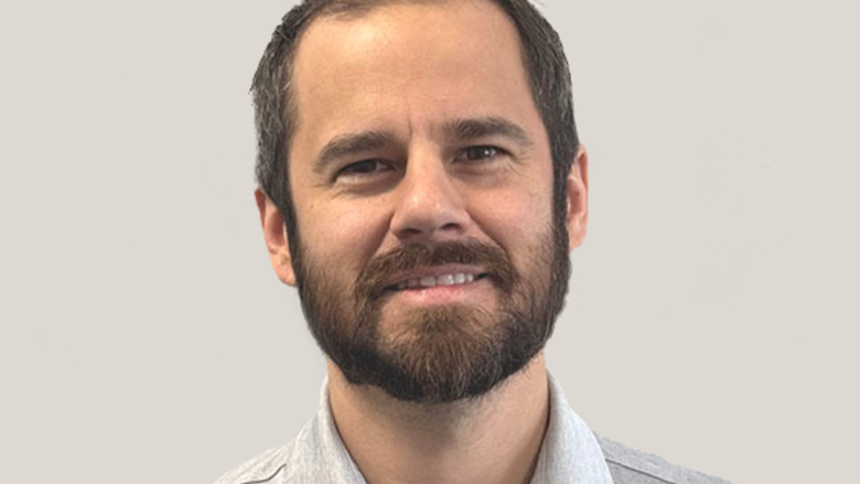 A headshot of a man against a light gray background.