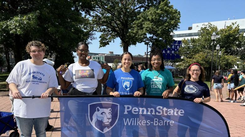 Five people standing outdoors holding a Penn State Wilkes-Barre banner.