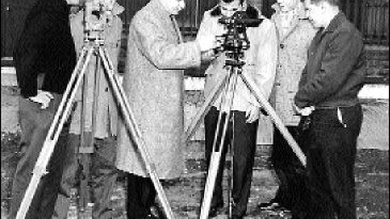 old black and white photo of men gathered around surveying equipment
