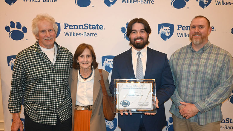 Four people standing against a backdrop with the Penn State Wilkes-Barre logo.