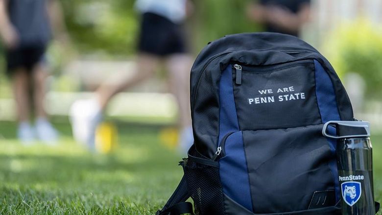 A backpack with the words "We Are Penn State" next to a water bottle with the Penn State logo sitting on a grassy field.