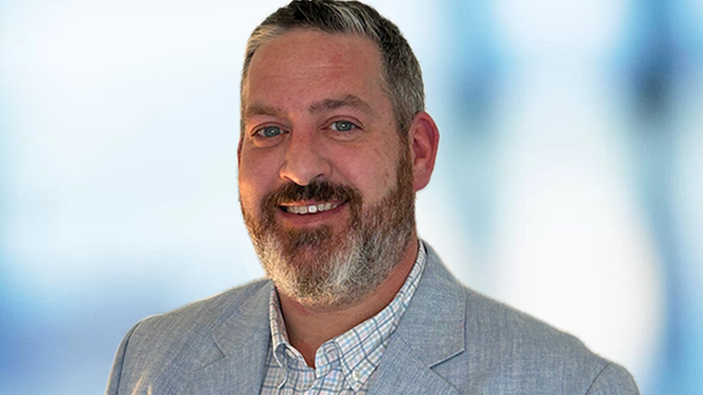 A headshot of a man with a beard wearing a light blue dress jacket