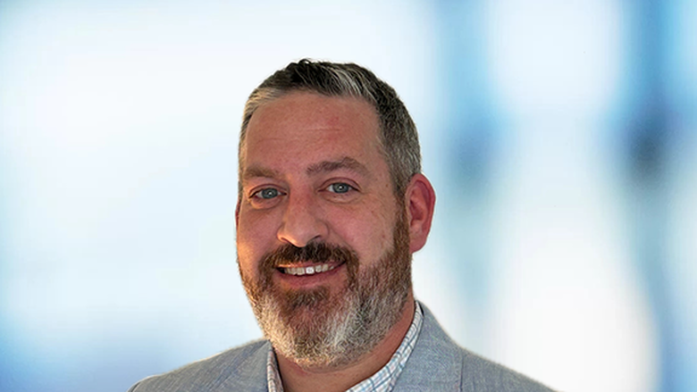 A headshot of a man with a beard wearing a light blue dress jacket