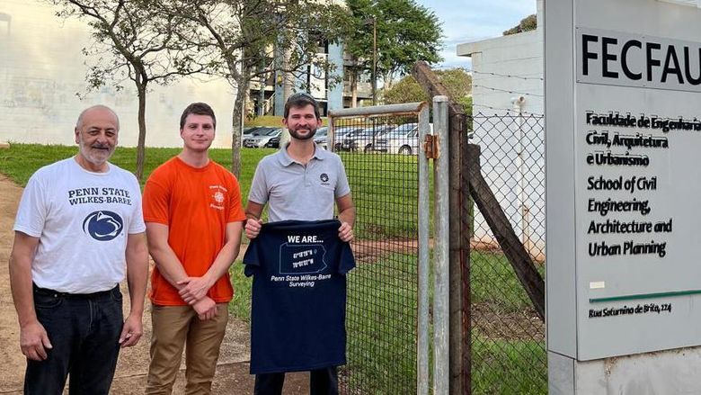 Three people, one holding a Penn State Wilkes-Barre shirt, stand outside a building in Brazil.