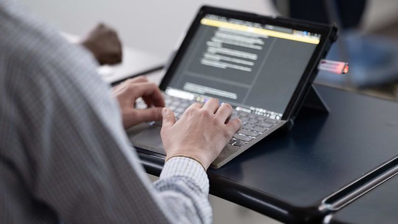 An image of the hands of someone who is seated and working on a laptop computer.