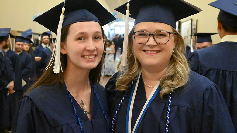 Two women in blue graduation caps and gowns standing next to each other.
