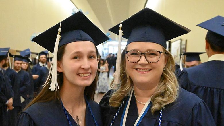 Two women in blue graduation caps and gowns standing next to each other.