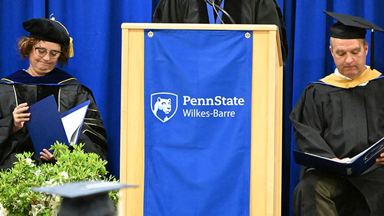 A woman in academic regalia speaks from the podium.