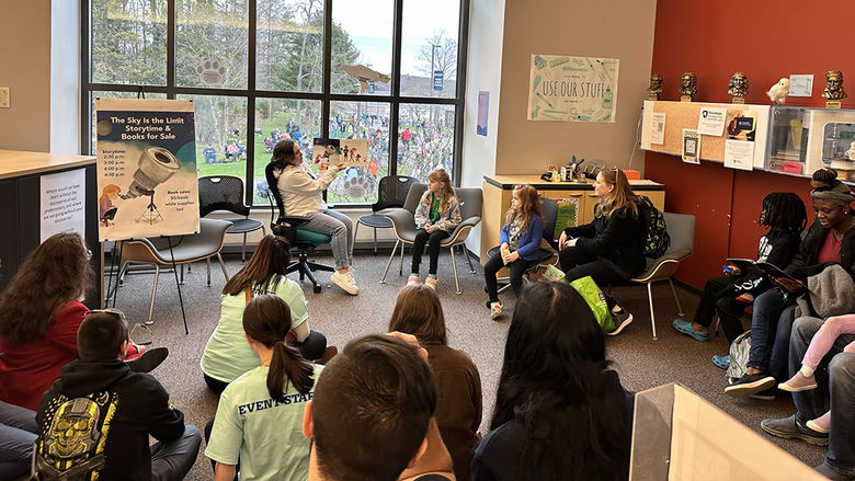 A woman holding up a book while reading a story to a room of people.