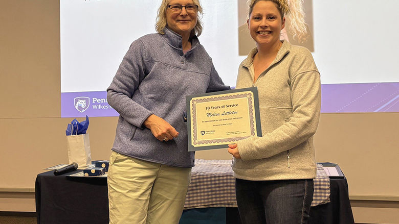 A woman at left presenting an award to a woman at right.