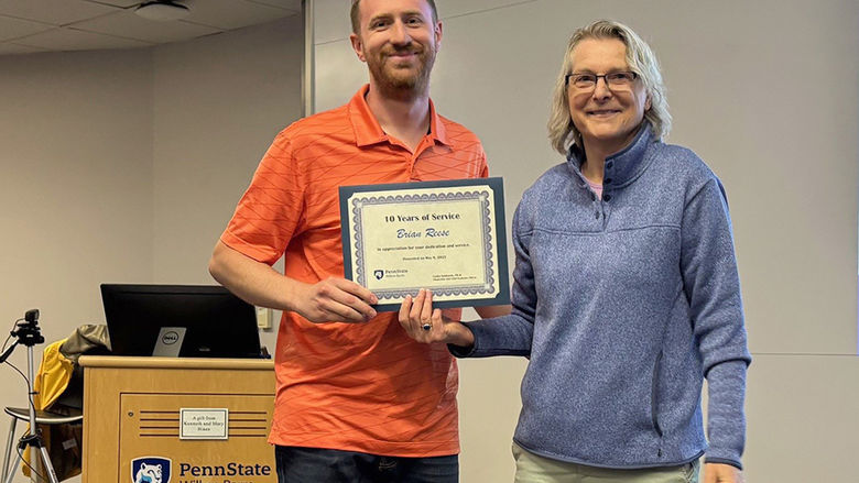A man at left receives an award from a woman at right.