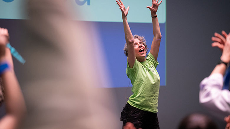 A woman dancing with her hands in the air at the front of a crowd.