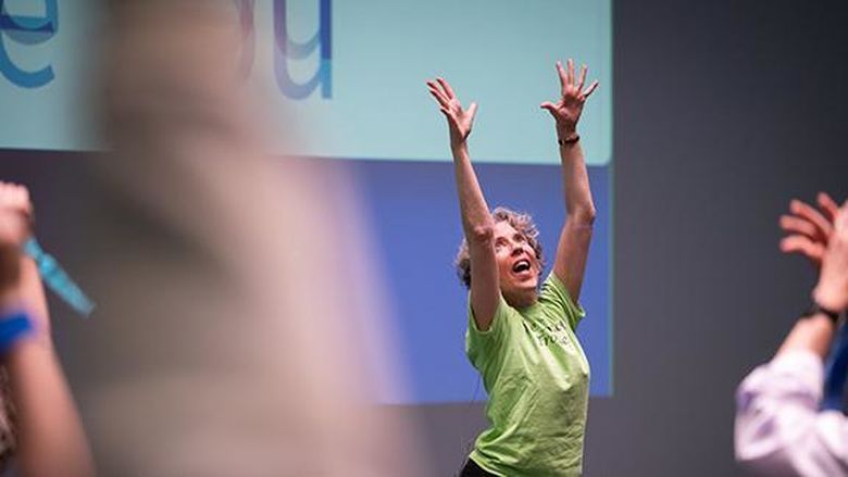 A woman dancing with her hands in the air at the front of a crowd.