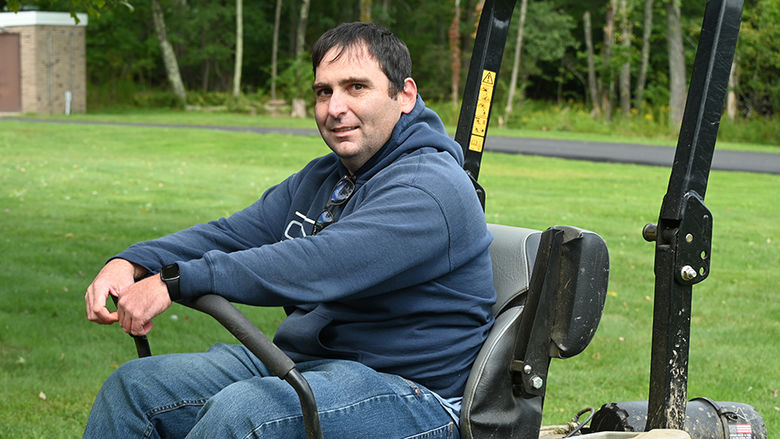 A man sitting on a riding lawn mower with the lawn behind him.