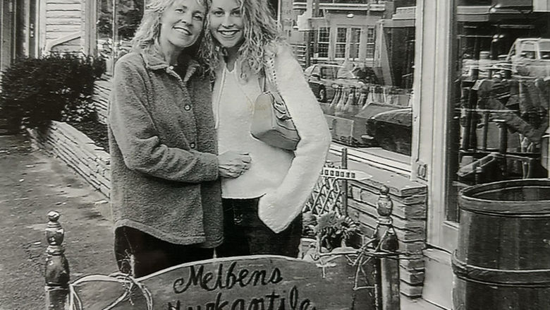 A black and white photo of two woman standing outside a business with their arms around each other.