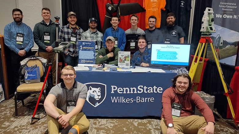 A large group of people gathered around a table with the Penn State Wilkes-Barre name and logo on a tablecloth.