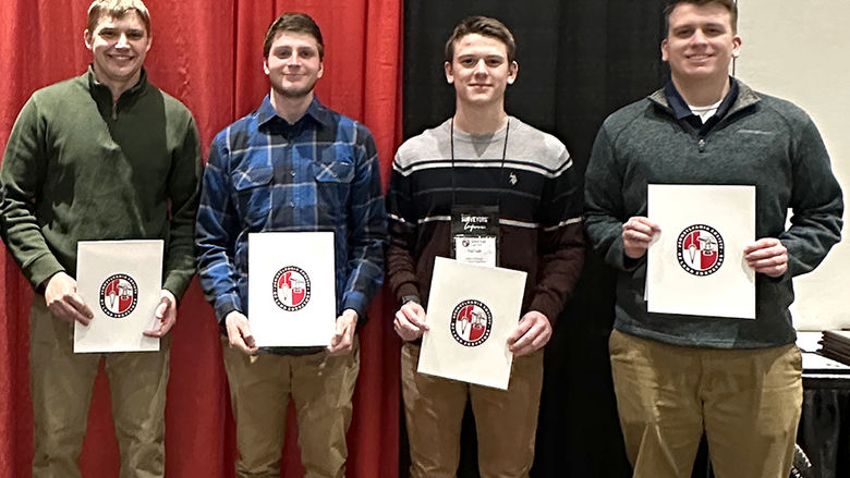 Four men standing holding certificates in honor of the scholarships they received.
