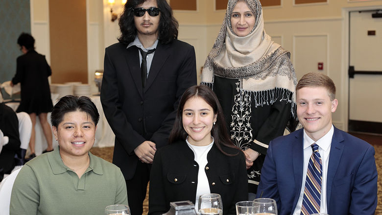 Three people seated at a table with two people standing behind them.