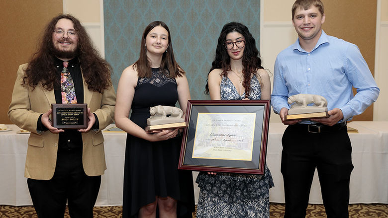 Four people standing alongside each other indoors, holding individual awards.