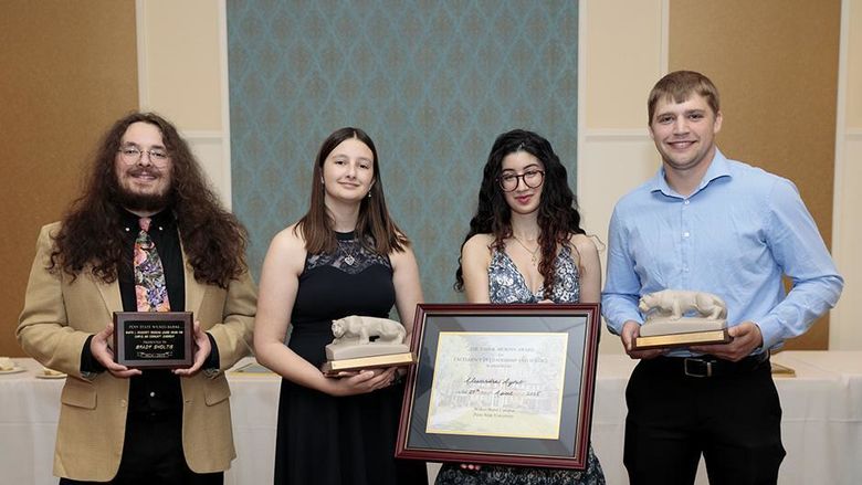 Four people standing alongside each other indoors, holding individual awards.