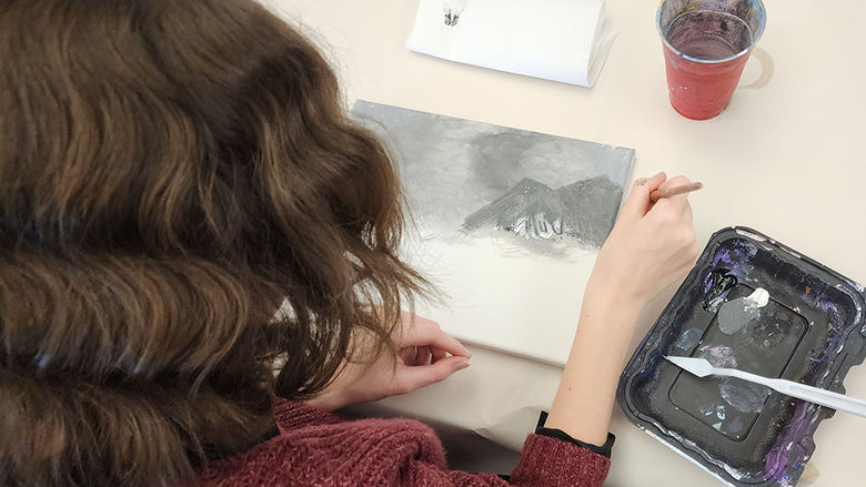 A photo taken behind a student sitting at a table painting.