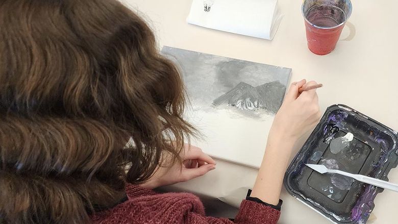 A photo taken behind a student sitting at a table painting.