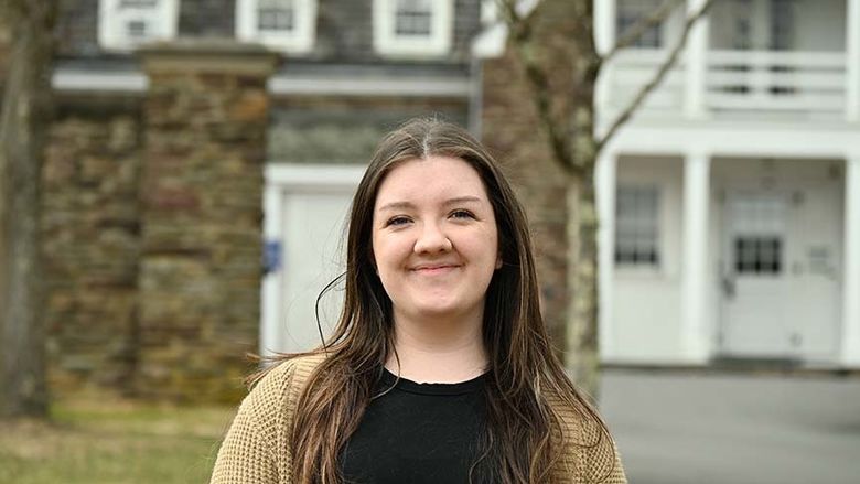 A female student stands outside in front of historic Hayfield House.