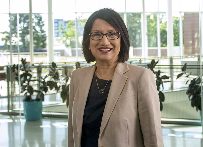 An image of Penn State President Neeli Bendapudi wearing a tan jacket while standing in a room filled with glass windows and sunlight