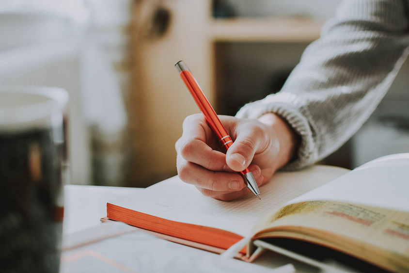 A hand holding a pen and writing in a book