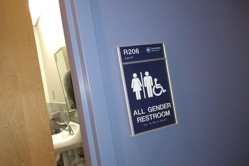 A partially open door to a single-stall bathroom with a sign stating "All Gender Restroom"