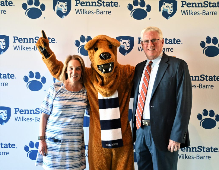 Two people standing with the Nittany Lion between them.