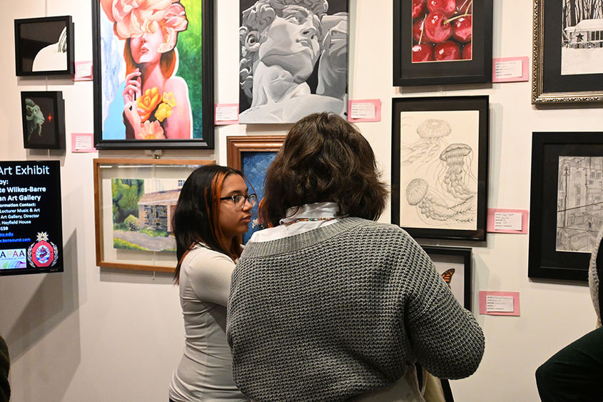 Two people talking while looking at a wall of gallery art.