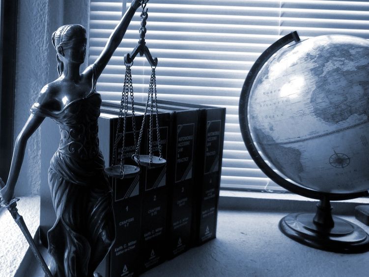 Lady Justice holding scales next to a globe placed on a desk.