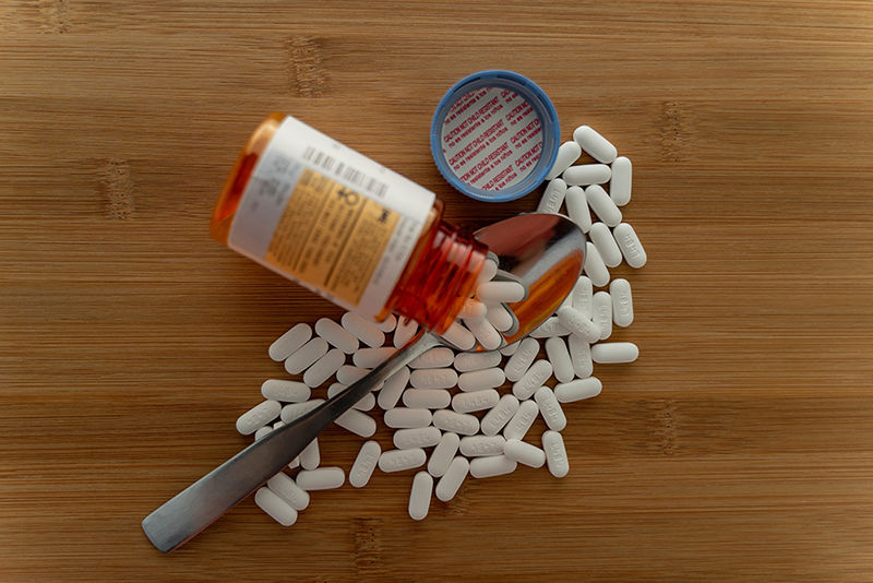 Prescription pills spilled out of the bottle onto a wooden table with a spoon
