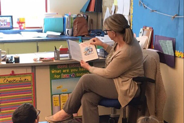 a volunteer reading a story to second graders sitting on the floor