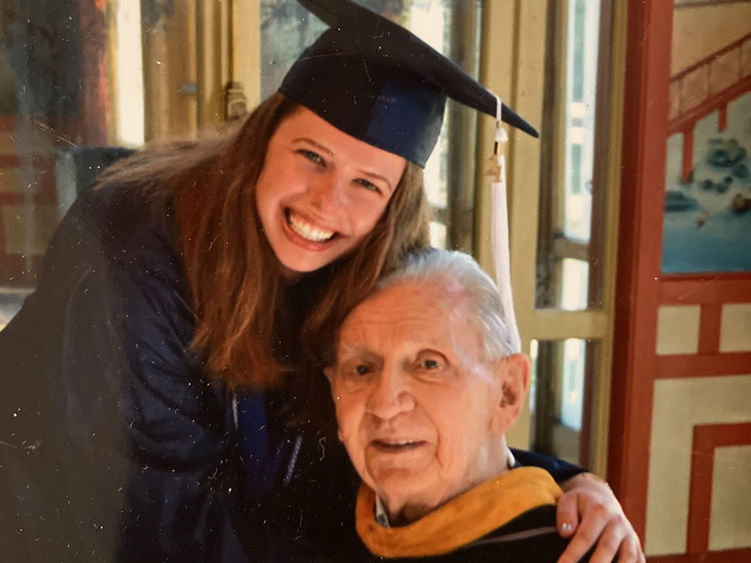 A woman in graduation regalia embraces her grandfather, also in regalia