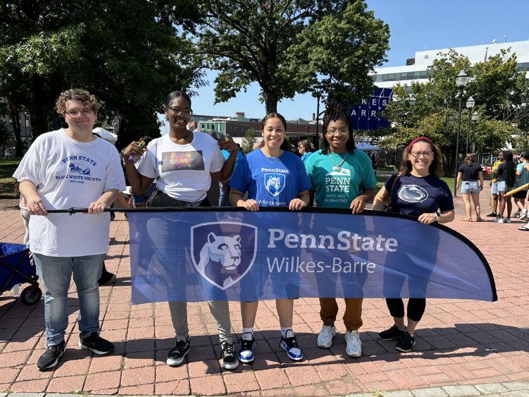 Five people standing outdoors holding a Penn State Wilkes-Barre banner.