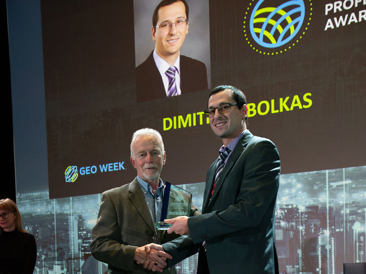 Two men standing, with one accepting an award from the other