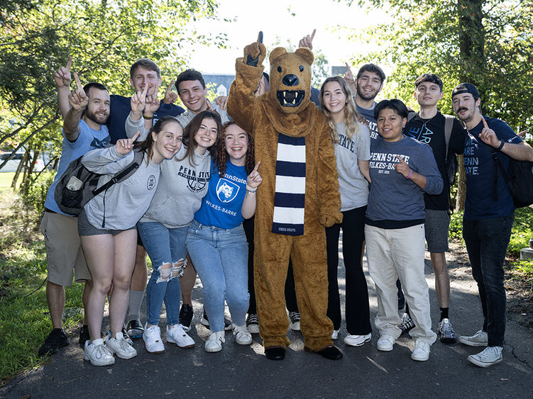 A large group of students in Penn State Wilkes-Barre clothing pose with the Nittany Lion on an outdoor walkway.