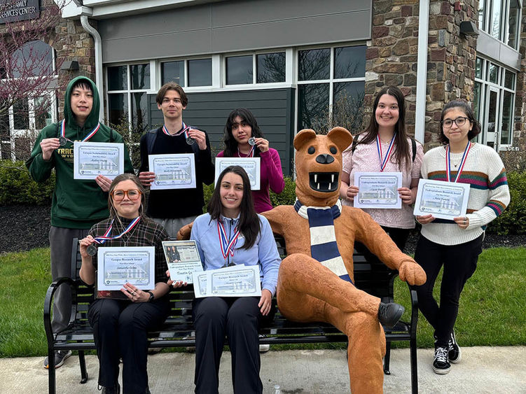 Students outdoors sitting on the Nittany Lion bench and behind the bench, holding their awards.