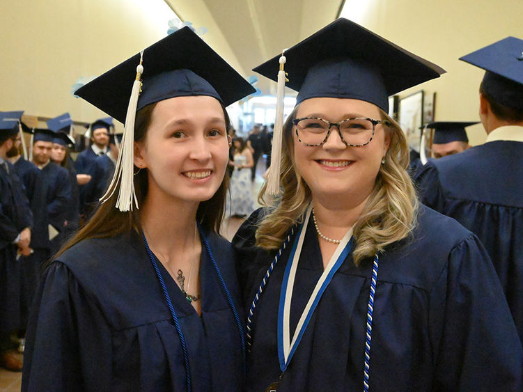 Two women in blue graduation caps and gowns standing next to each other.