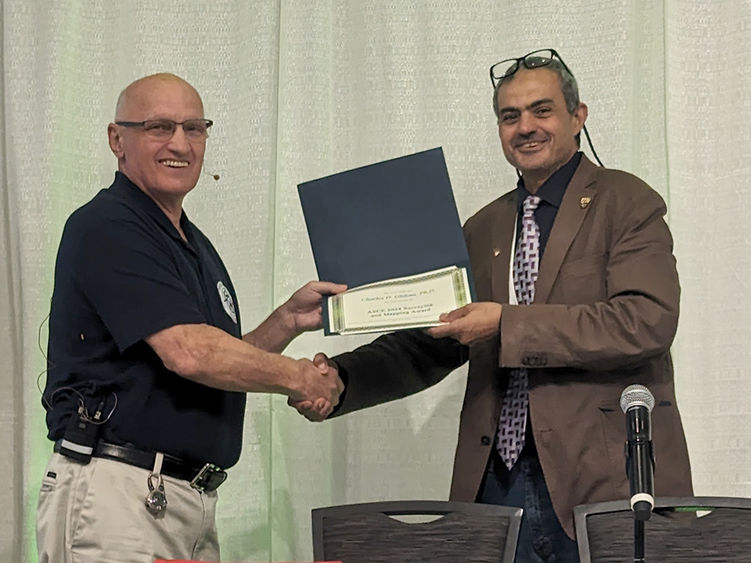 A man at right presenting an award to a man at left.