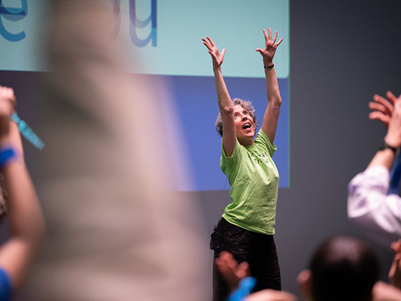 A woman dancing with her hands in the air at the front of a crowd.