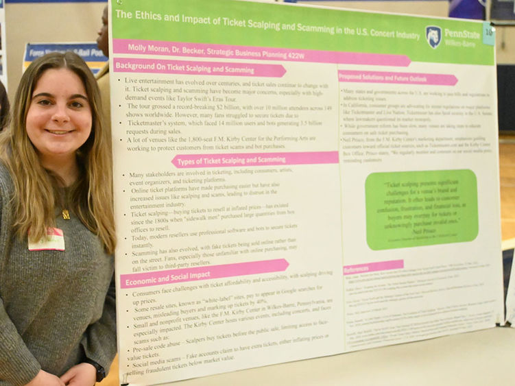 A woman stands at left next to a large research poster on a table.